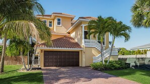A two-story house with a brown garage door, a white railing on the second floor, and a paved driveway. - Paradise in Naples (Naples)