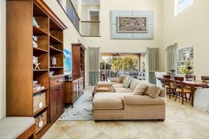 Relax in this spacious living area with a high ceiling and balcony, featuring a comfortable sofa, bookshelf, and dining table.