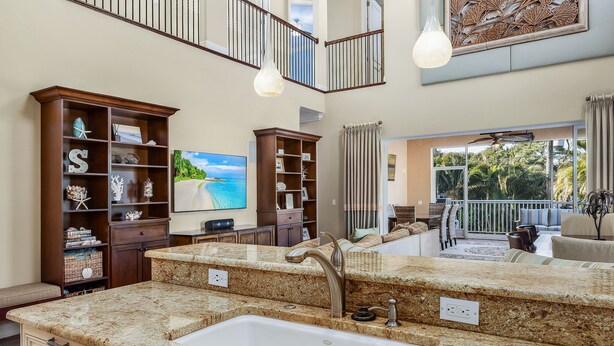 A spacious kitchen with granite countertops, a double sink, and a large island. There are built-in bookshelves and a flat-screen TV. - Paradise in Naples (Naples)