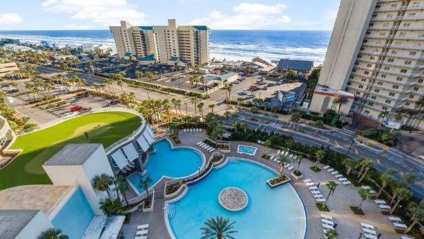 A resort with a large pool, palm trees, and a view of the ocean. - SMOOTH SAILING-BEAUTIFULLY DECORATED, GULF VIEWS (Panama City Beach)