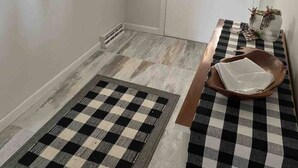 Une salle de bain avec un carrelage à motifs, un porte-serviettes avec des serviettes blanches, une porte avec une fenêtre et une petite table sur laquelle se trouvent un bol et un vase.