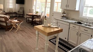 Une cuisine avec des meubles blancs, une table en bois et un coin repas avec des chaises.
