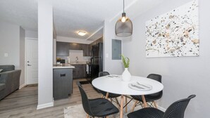 A modern kitchen with dark cabinets, a refrigerator, and a dining area with a round table and black chairs. - Shopping Paradise | Free coffee + Parking (Kettering)