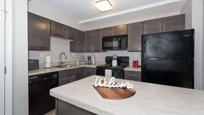 A modern kitchen with dark cabinets, a black refrigerator, a microwave, a stove, and a coffee maker. - Shopping Paradise | Free coffee + Parking (Kettering)