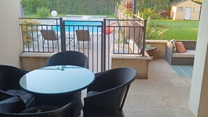 Un patio couvert avec une piscine, du mobilier d’extérieur et une vue sur le jardin arrière.
