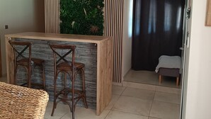 Une cuisine moderne avec un îlot central en bois, deux tabourets de bar, un jardin vertical vert et un rideau foncé en arrière-plan.