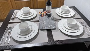 Una mesa de comedor dispuesta con platos, fuentes y cubiertos blancos, una botella de vino y dos vasos de agua.