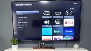 Televisor de pantalla plana montado en un mueble blanco, mostrando una interfaz de Roku TV con varios servicios de transmisión.
