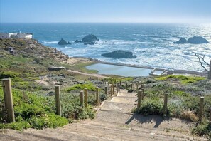 Eine Küstenansicht mit einer Treppe, die zu einem Strandabschnitt führt, mit Felsformationen und ruhiger See.