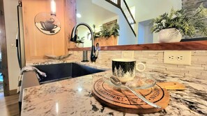 A kitchen with a marble countertop, a coffee maker, a sink, and a decorative plate.