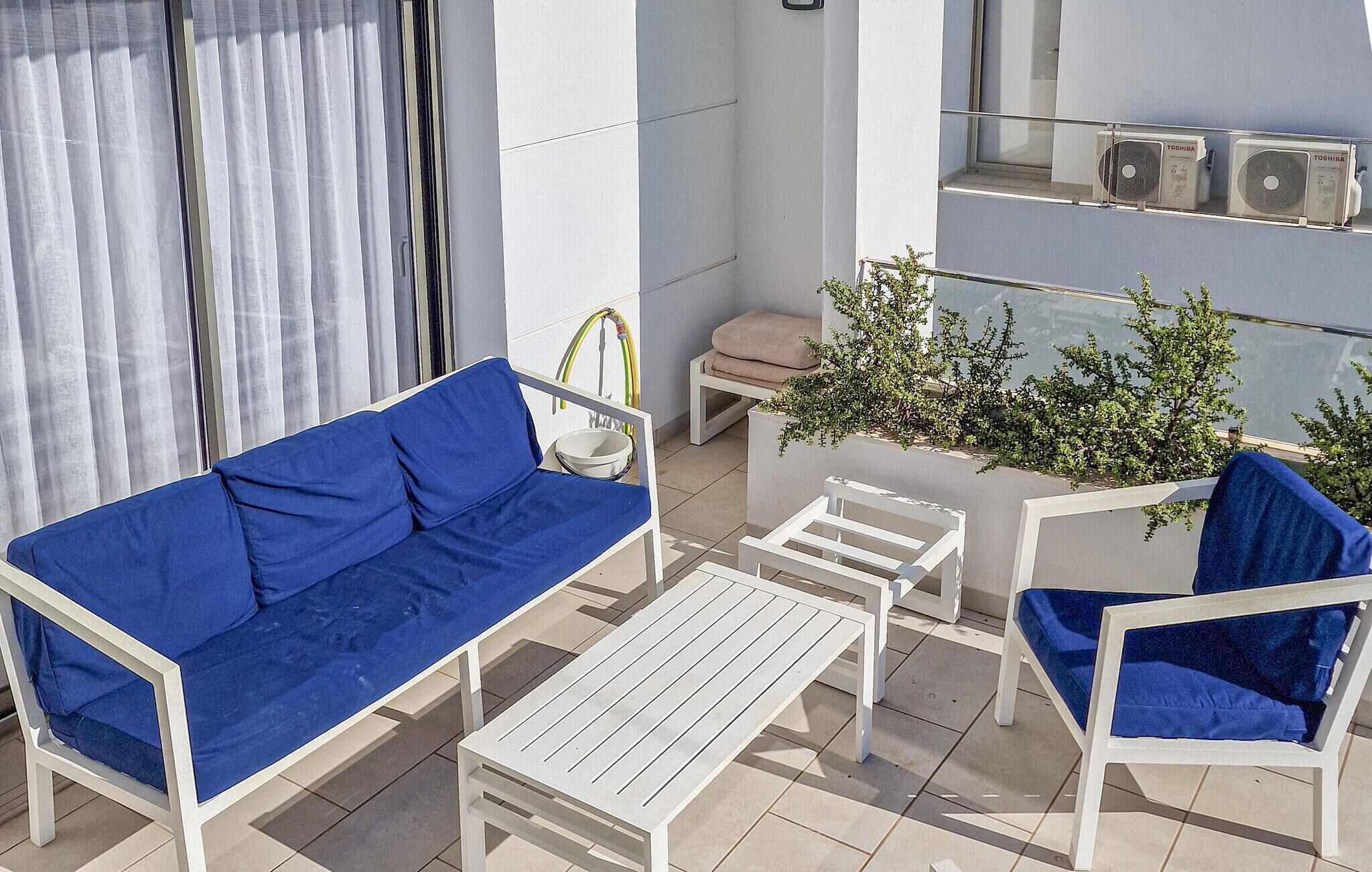 A balcony with a blue sofa, white chairs, a small table, and a potted plant.