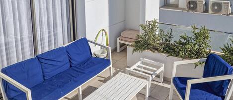 A balcony with a blue sofa, white chairs, a small table, and a potted plant.