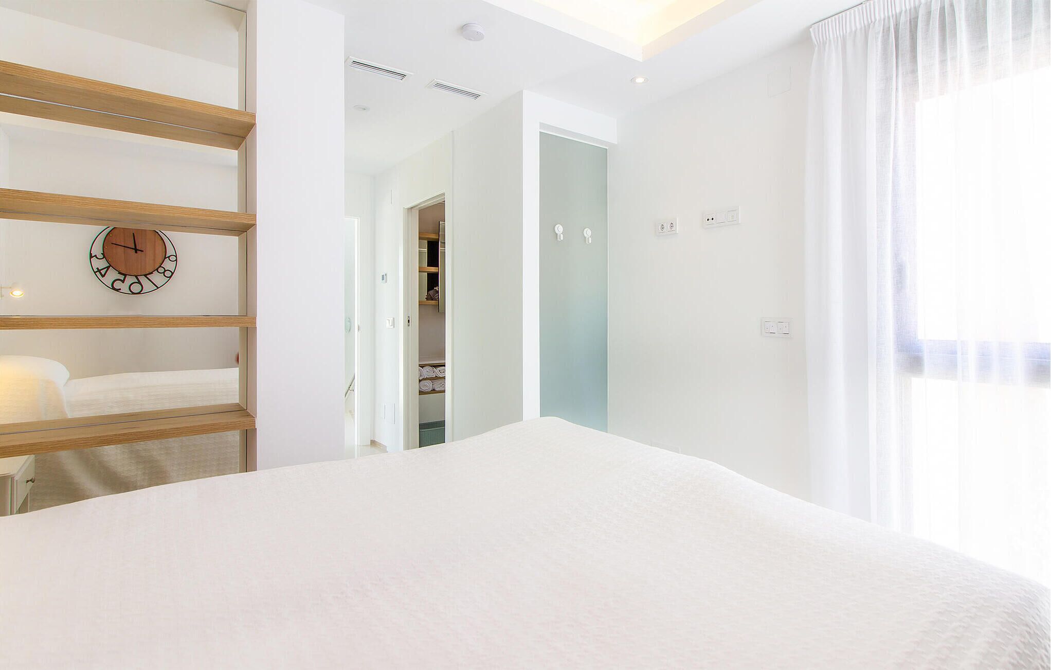 Une chambre à coucher moderne avec un grand lit, une horloge en bois accrochée au mur et un dressing.