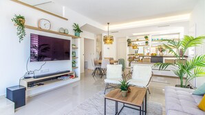 Un salon moderne doté d’un téléviseur à écran plat, d’étagères en bois et d’un coin repas agrémenté d’un lustre.
