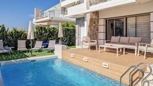Un espace piscine extérieur moderne, doté d’une terrasse en bois, de chaises longues et d’un canapé.