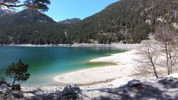 Un llac translúcid amb una platja sorrenca, envoltat de muntanyes boscoses.