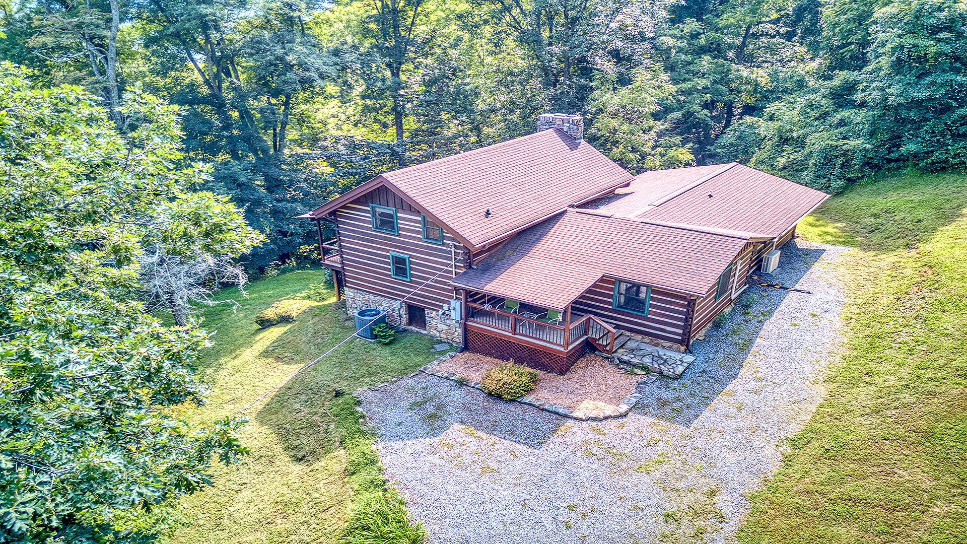 A two-story log cabin with a porch and a chimney, surrounded by dense forest.