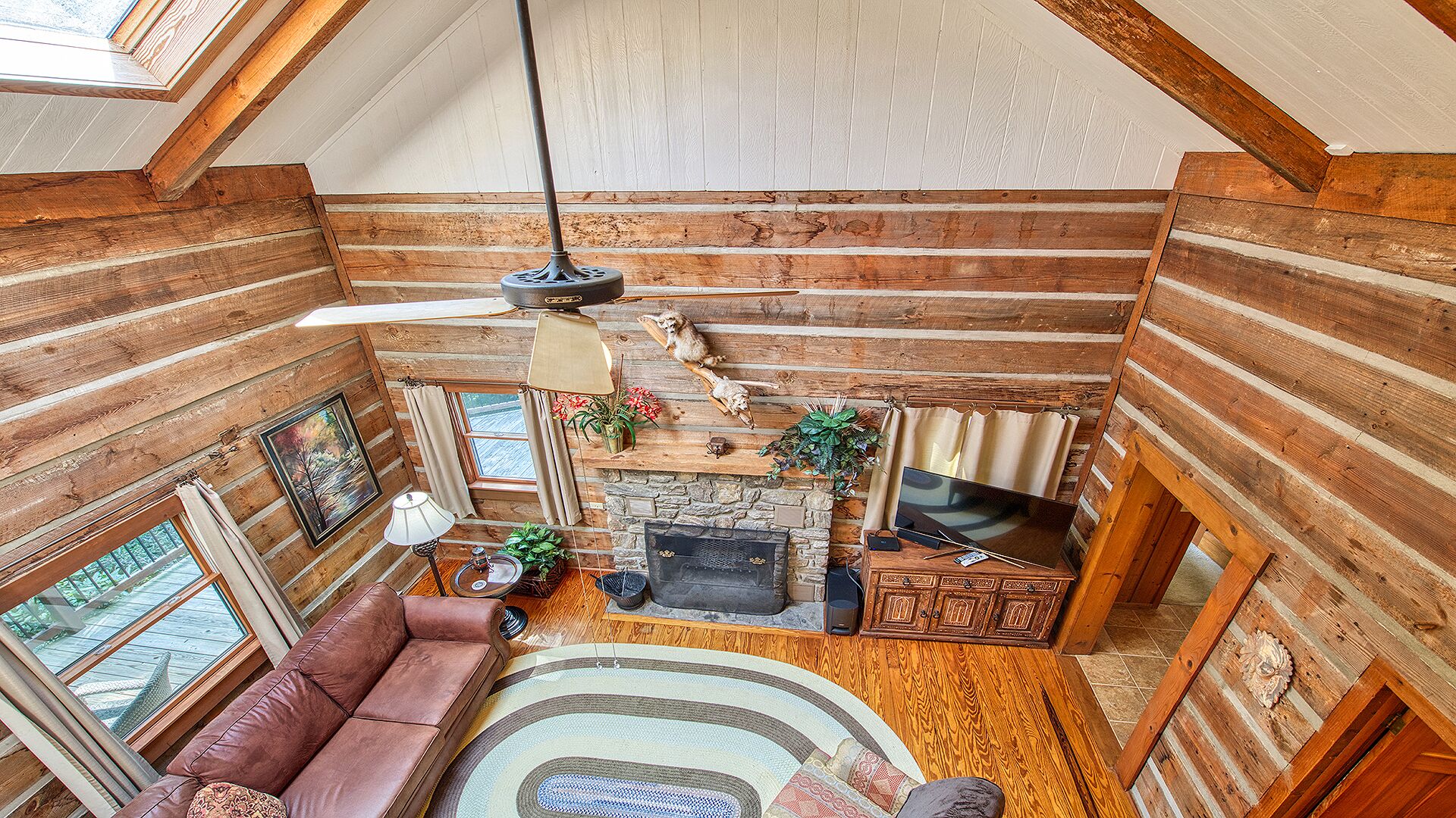 A log cabin interior with a stone fireplace, leather sofa, and a television.