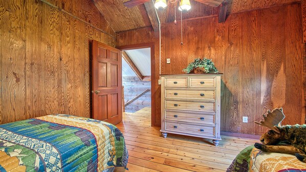 Un interior de madera con una cama, un aparador y vista de una escalera de madera.