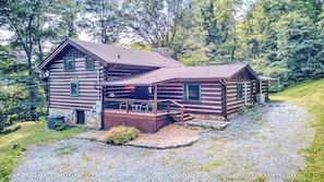 A log cabin with a porch, a chimney, and a stone foundation.