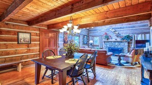 A log cabin interior with a dining area, fireplace, and cozy seating.