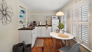 A compact kitchen with white cabinets, a dining table with chairs, a hanging light fixture, and a large window with shutters. - Location! Location! Location! In the middle of Downtown Mt Dora!  (Mount Dora)