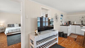 A modern, well-lit room with a bed, a TV on a white console, a kitchen area with white cabinets, and a dining table. - Location! Location! Location! In the middle of Downtown Mt Dora!  (Mount Dora)