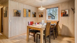 Un comedor con una mesa y sillas de madera, una lámpara colgante y cuadros en las paredes.