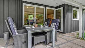 Un patio exterior con una mesa y cuatro sillas, un bote de basura y una puerta corrediza de vidrio que da a una cocina.