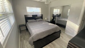 Une chambre à coucher avec un lit, des tables de chevet, un miroir et une fenêtre avec des stores.