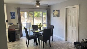 Un espace repas comprenant une table et des chaises, un ventilateur de plafond, une porte et une fenêtre avec des rideaux.