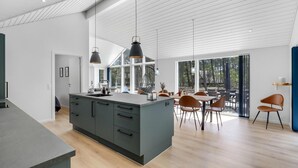 Una cocina moderna con una isla grande, comedor con sillas y amplios ventanales que ofrecen vistas al exterior.