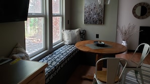 Una habitación acogedora con un ventanal grande, una mesa redonda de madera, un banco y un televisor en la pared.
