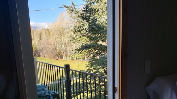 Una habitación con una cama, una terraza de madera y vistas a un paisaje verde con árboles y una cerca.