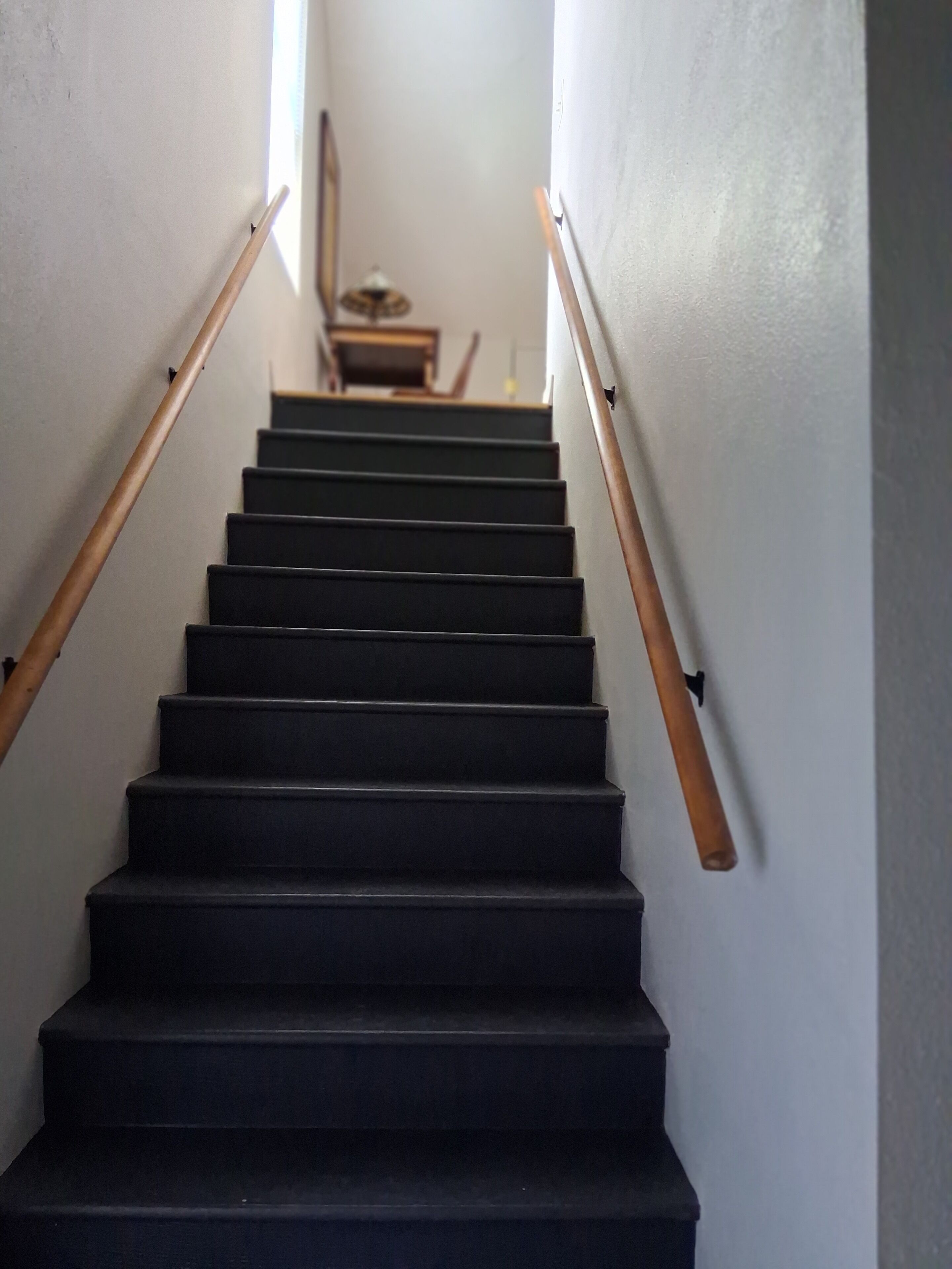 Un escalier avec des rampes en bois et des marches noires menant à un palier où se trouvent une petite table et une lampe.