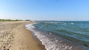 Ein sandiger Strand mit sanften Wellen, einem klaren Himmel und Gebäuden in der Ferne.