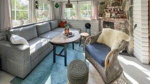 Una sala de estar acogedora con un sofá gris, un sillón azul, una mesa de centro redonda de madera y una chimenea de piedra.