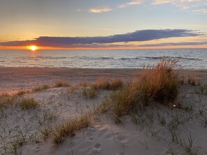 Une plage avec du sable et de l’herbe au premier plan, et l’océan en arrière-plan.