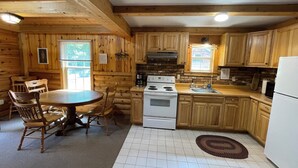 Una cocina estilo cabaña con paredes de madera, una mesa redonda y electrodomésticos básicos.