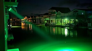 Propiedad frente al agua de noche, con edificios iluminados y zona de piscina con luz verde.