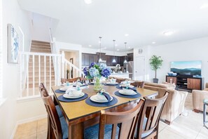 A dining area with a wooden table set for four, a staircase, and a kitchen in the background.