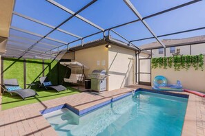 An indoor pool area with a grill, lounge chairs, and a covered seating area.