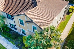 A multi-story building with a tiled roof, multiple windows, and a well-maintained lawn with palm trees.