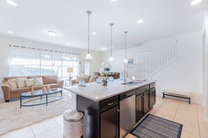 A modern kitchen with a central island, a dining area with a sofa, and a staircase leading to another level. - Large Home w/ Private pool, Clubhouse, Near Parks (Kissimmee)