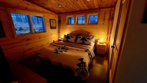 Un dormitorio de cabaña de madera con una cama, almohadas y una mesita de noche.
