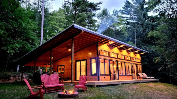 Una baita di legno con veranda coperta, ampie finestre e un braciere.