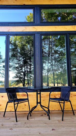 Una mesa de madera con dos sillas frente a amplios ventanales que dan a un paisaje de árboles.