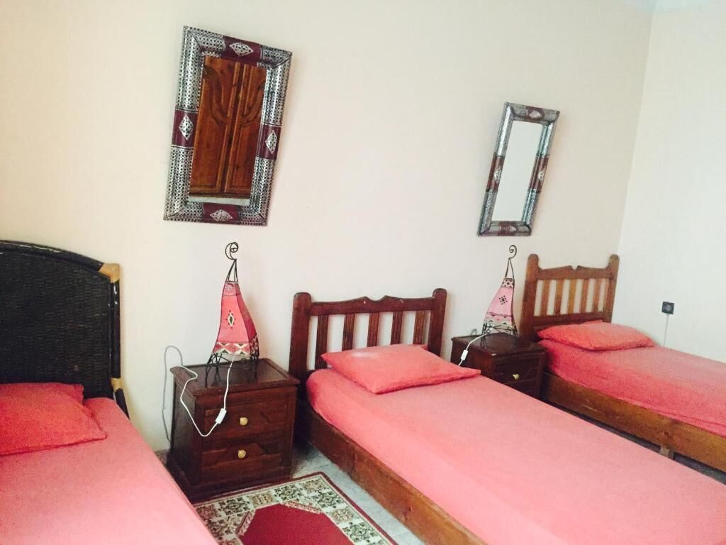A bedroom with two single beds, a wooden headboard, a nightstand with a lamp, and a mirror on the wall.