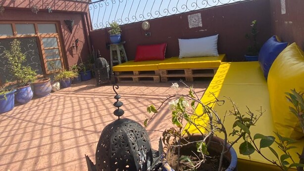 A covered patio area with a yellow sofa and cushions, potted plants, and a decorative metal lantern.