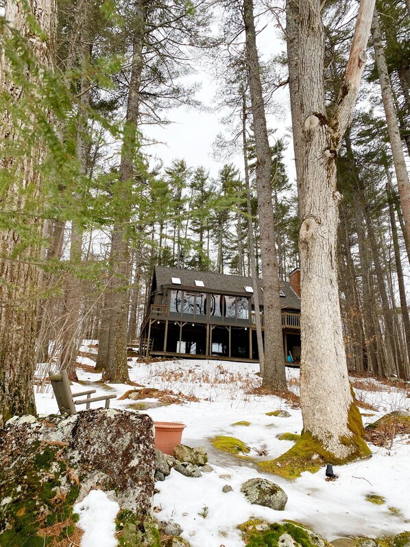 A cabin with a large deck, surrounded by tall trees and snow-covered ground.